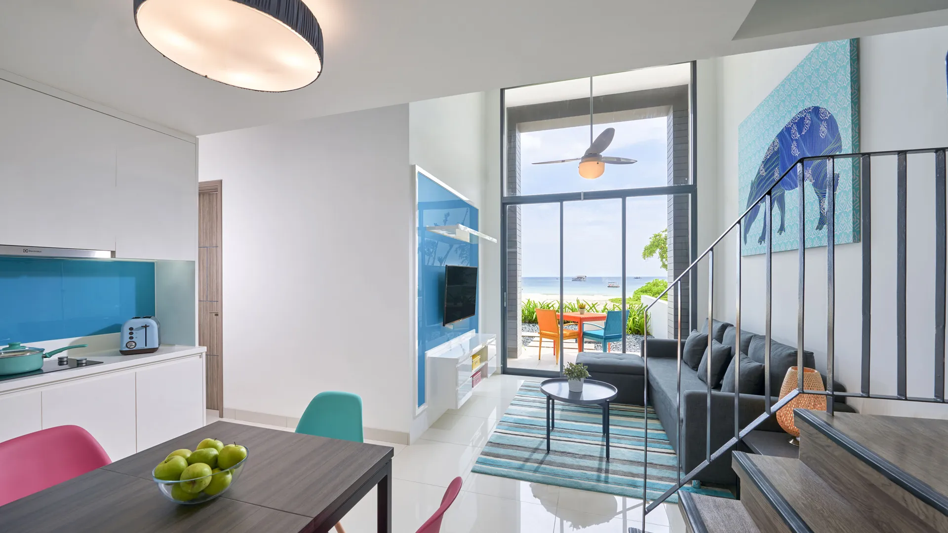 แคสเซีย เรสซิเดนซ์ บินตัน | A modern, brightly-lit living space with a dining area and kitchen leading to an outdoor patio overlooking the sea.